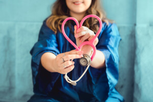 Nurse dressed in blue holding a stethoscope with a heart shape tube in red